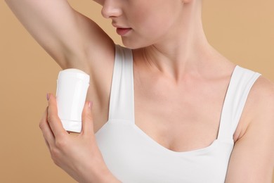 Photo of Woman applying deodorant on beige background, closeup