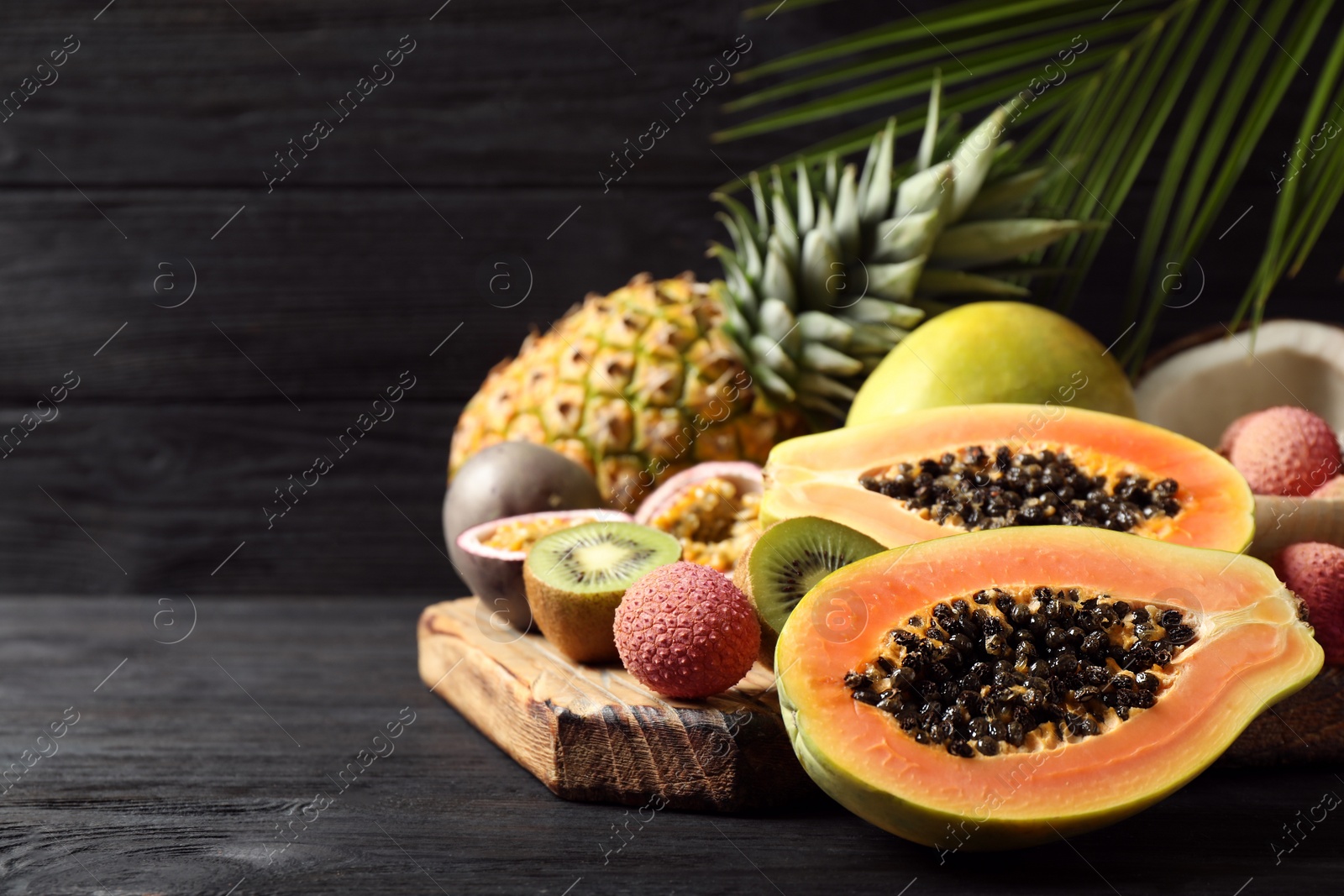 Photo of Fresh ripe papaya and other fruits on dark wooden table. Space for text
