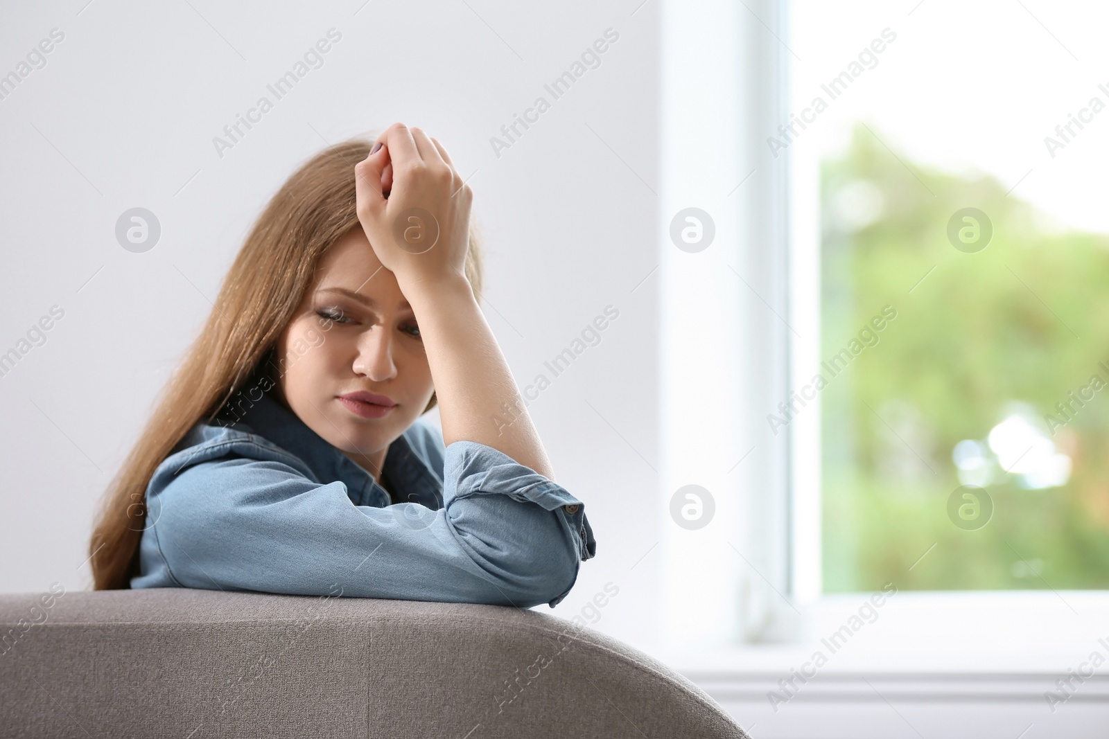 Photo of Young sad woman sitting near window at home