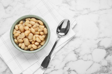 Photo of Bowl of canned kidney beans and spoon on white marble table, top view. Space for text