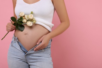 Photo of Pregnant woman with roses on pink background, closeup. Space for text