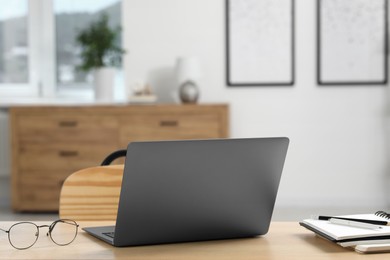 Photo of Home workspace. Laptop, glasses and stationery on wooden desk in room