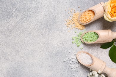 Scoops with different sea salt and flowers on light grey table, flat lay. Space for text