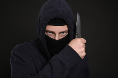 Photo of Man in mask with knife on black background. Dangerous criminal