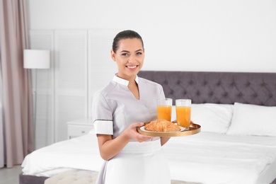 Photo of Young chambermaid holding tray with breakfast in bedroom