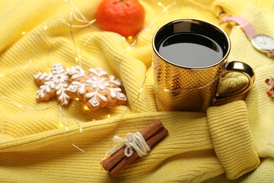 Cup of hot drink with gingerbread cookies and Christmas lights on yellow sweater