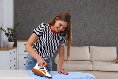 Young woman ironing clothes on board at home. Space for text