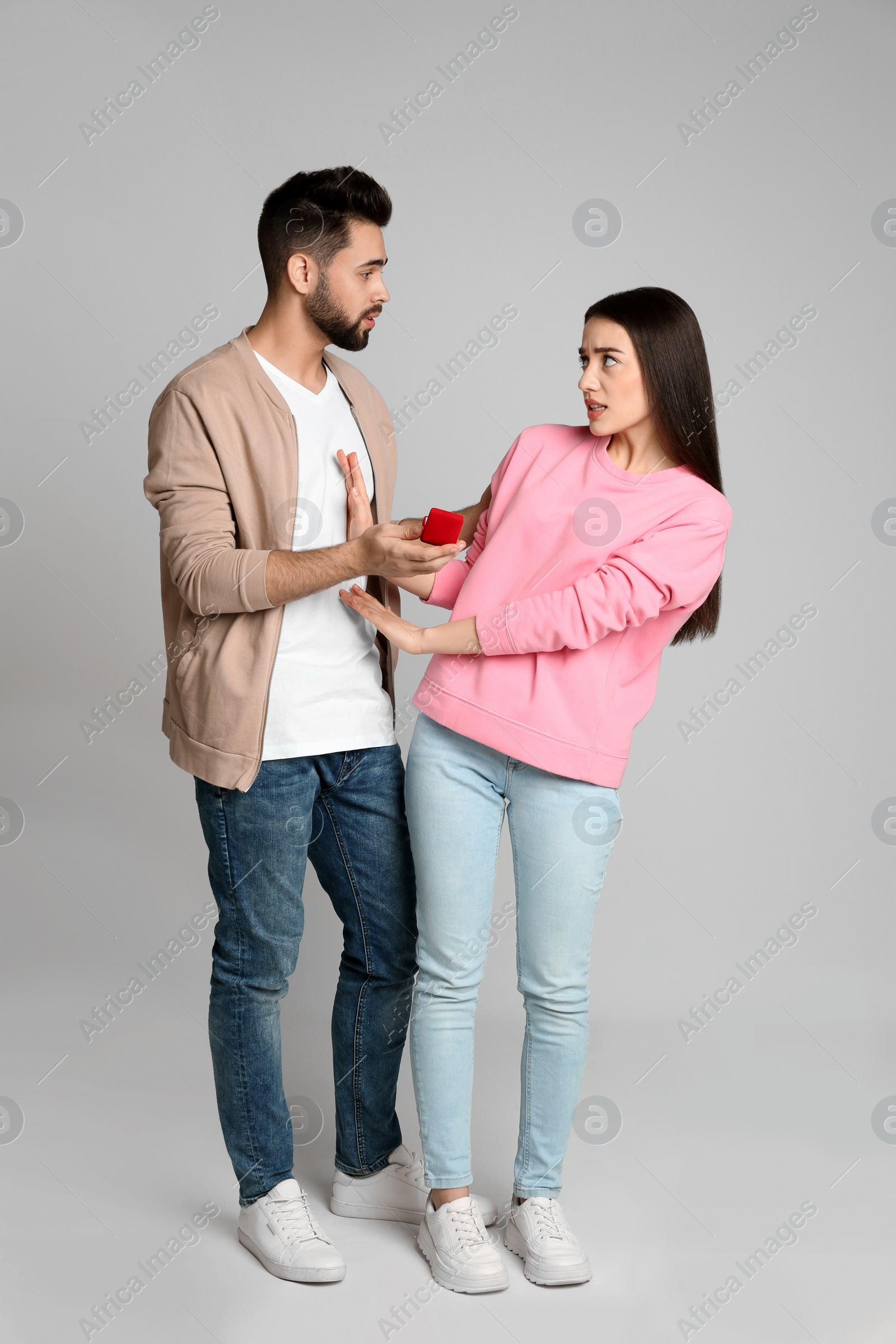 Photo of Young woman rejecting engagement ring from boyfriend on light grey background