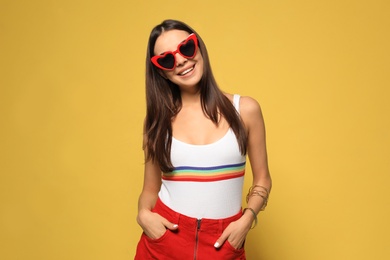 Photo of Portrait of beautiful young woman with heart shaped sunglasses on color background