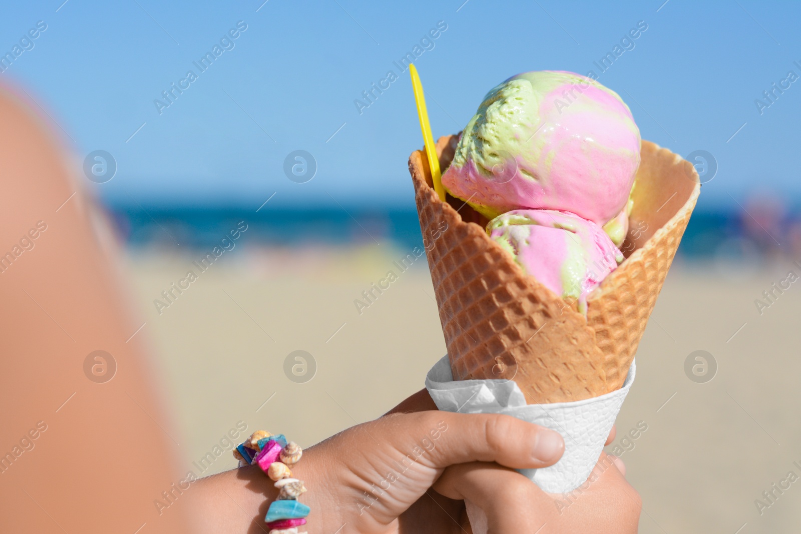 Photo of Little girl holding waffle cone with scoops of delicious colorful ice cream at beach on sunny summer day, closeup. Space for text