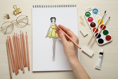 Image of Fashion designer creating new look. Woman drawing sketch in pad with pencil at white wooden table, top view