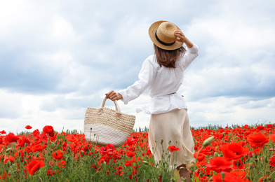 Woman with straw hat and handbag in blooming poppy field