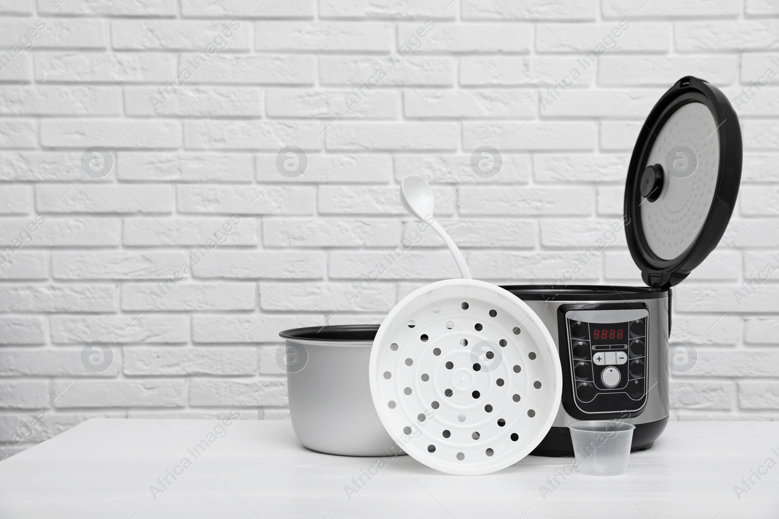 Photo of Modern electric multi cooker, parts and accessories on table near brick wall. Space for text