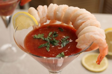 Photo of Tasty shrimp cocktail with sauce in glass and lemon on blurred background, closeup