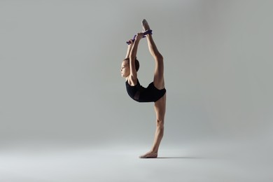 Photo of Cute little gymnast with rope doing standing split on white background