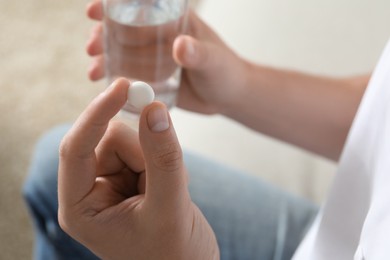 Man with glass of water and pill on blurred background, closeup