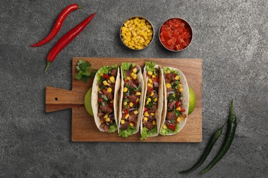 Delicious tacos with meat and vegetables on gray textured table, flat lay