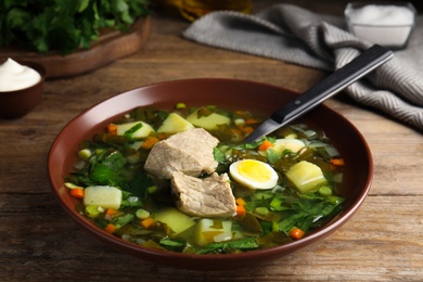 Photo of Delicious sorrel soup with meat and egg served on wooden table