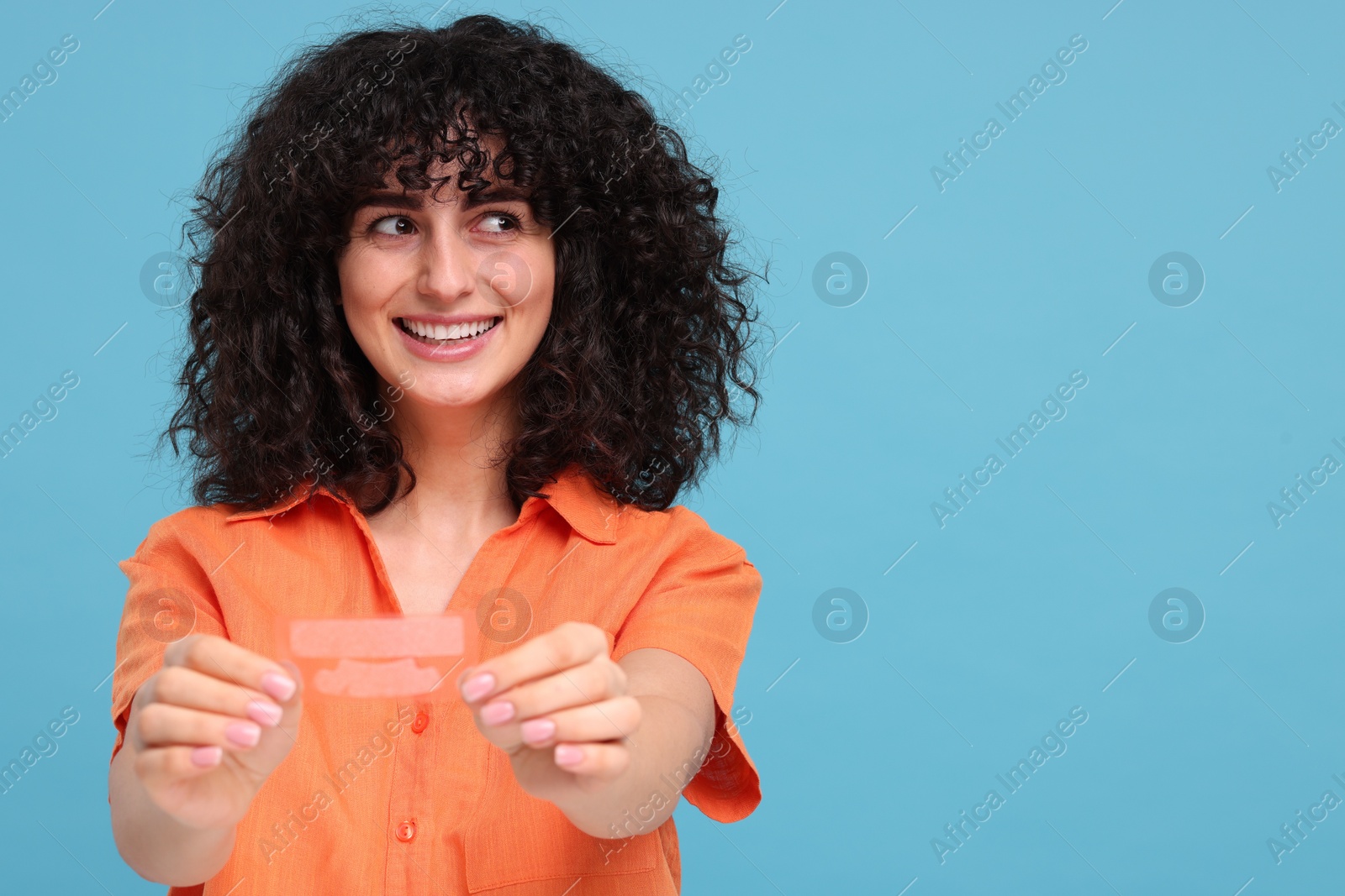 Photo of Young woman holding teeth whitening strips on light blue background, space for text