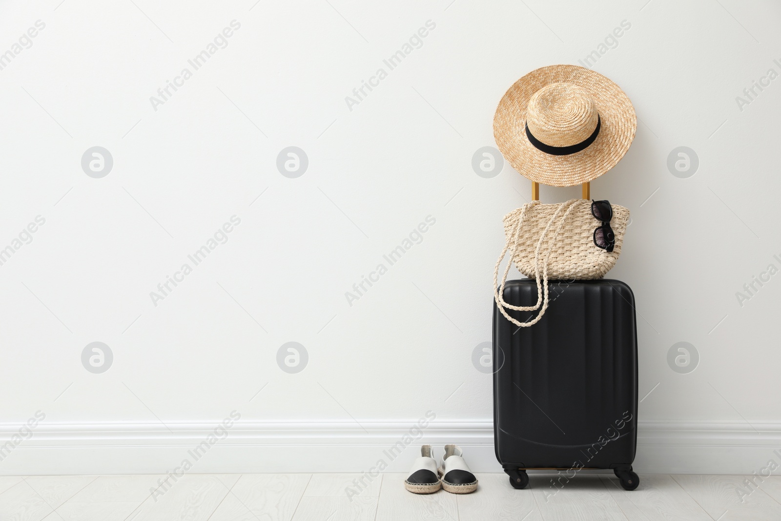 Photo of Packed suitcase, shoes and summer accessories near white wall indoors. Space for text