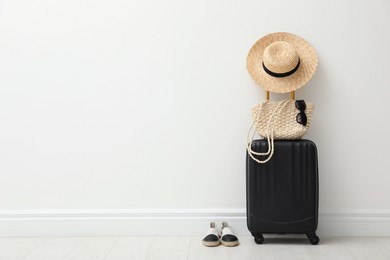 Packed suitcase, shoes and summer accessories near white wall indoors. Space for text