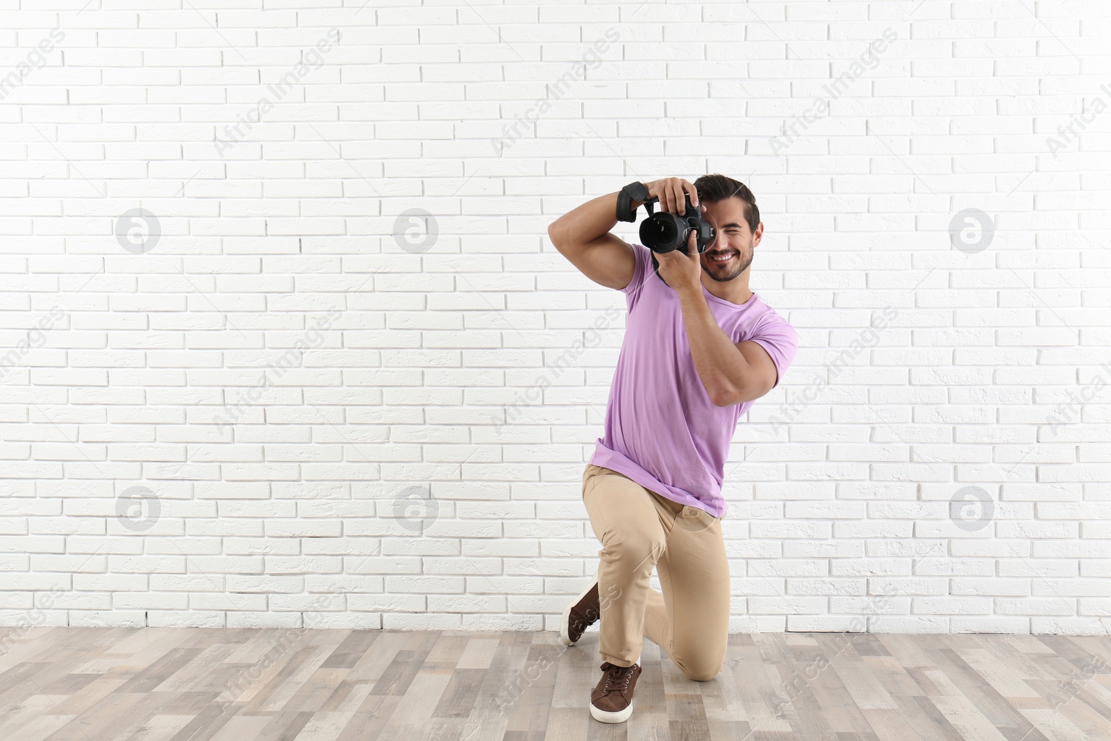 Photo of Young professional photographer taking picture near brick wall. Space for text