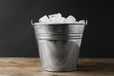 Photo of Metal bucket with ice cubes on wooden table