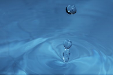 Photo of Drop falling into water on blue background, macro view. Space for text