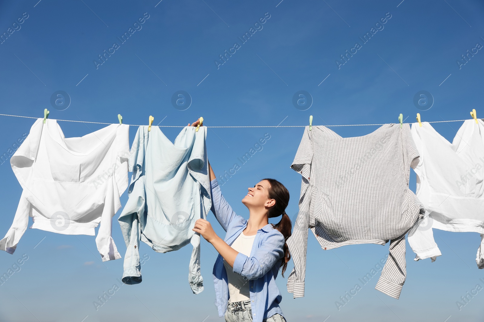 Photo of Woman hanging clothes with clothespins on washing line for drying against blue sky