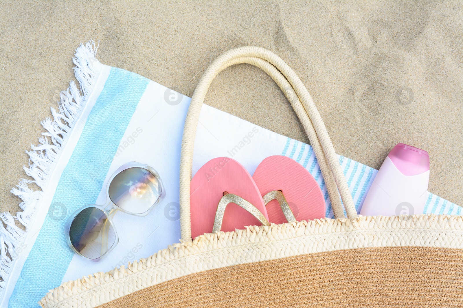 Photo of Striped towel with beach accessories on sand, flat lay