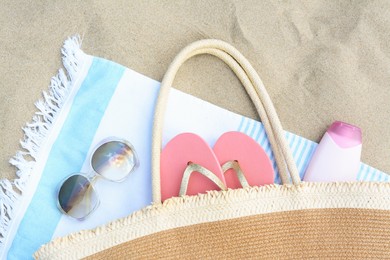 Striped towel with beach accessories on sand, flat lay