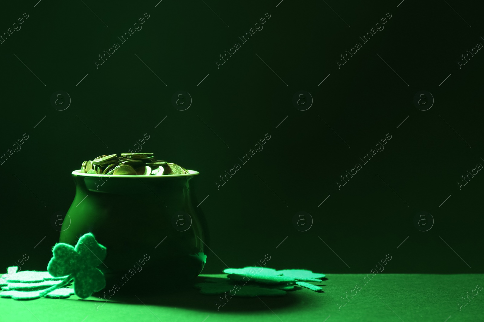 Photo of Pot of gold coins and clover leaves on green table against dark background, space for text. St. Patrick's Day celebration