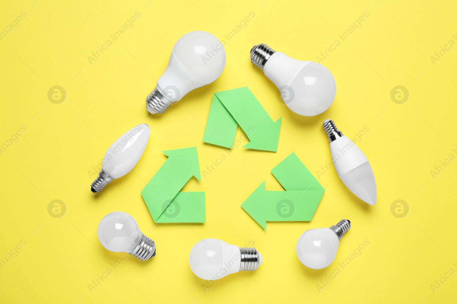 Photo of Recycling symbol and light bulbs on yellow background, flat lay