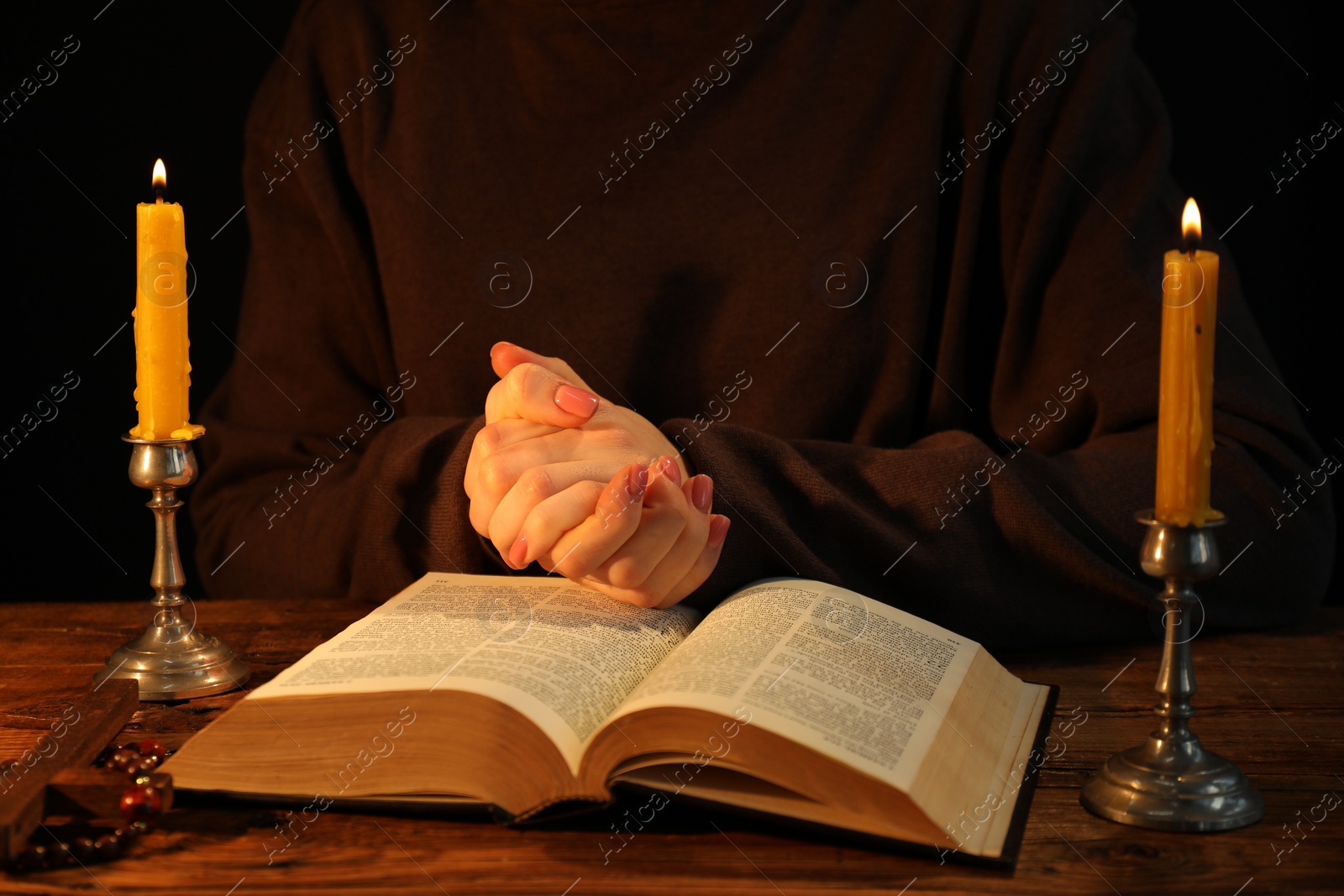 Photo of Woman praying at table with burning candles and Bible, closeup