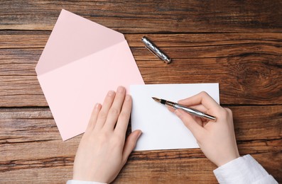 Photo of Woman writing letter at wooden table, top view