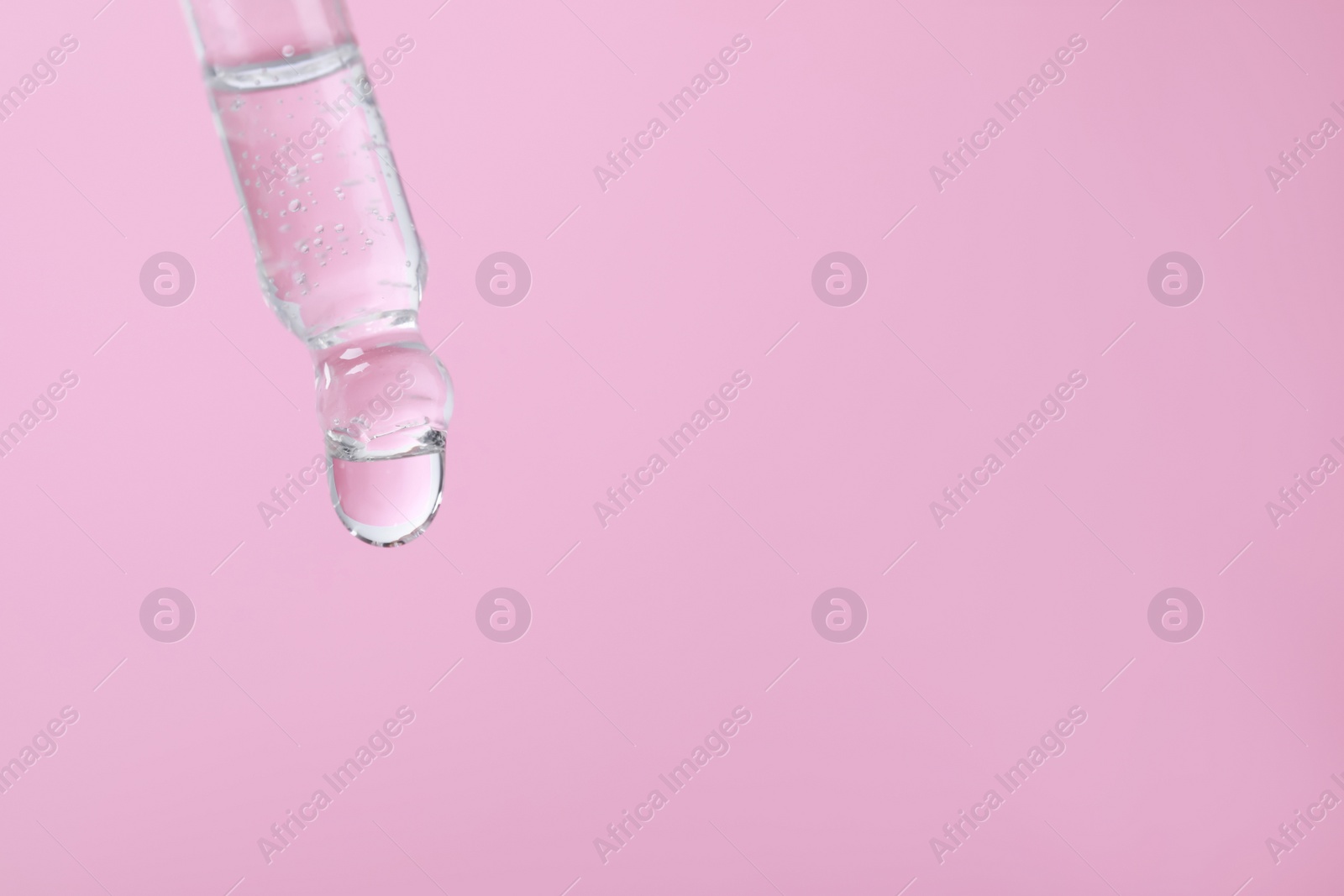 Photo of Dripping serum from pipette on pink background, closeup. Space for text