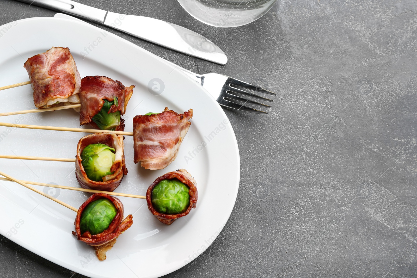 Photo of Brussels sprouts wrapped in bacon served on grey table, flat lay. Space for text