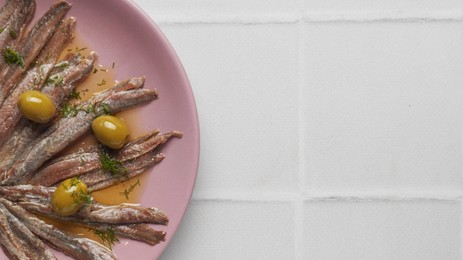 Photo of Canned anchovy fillets with olives on white tiled table, top view. Space for text
