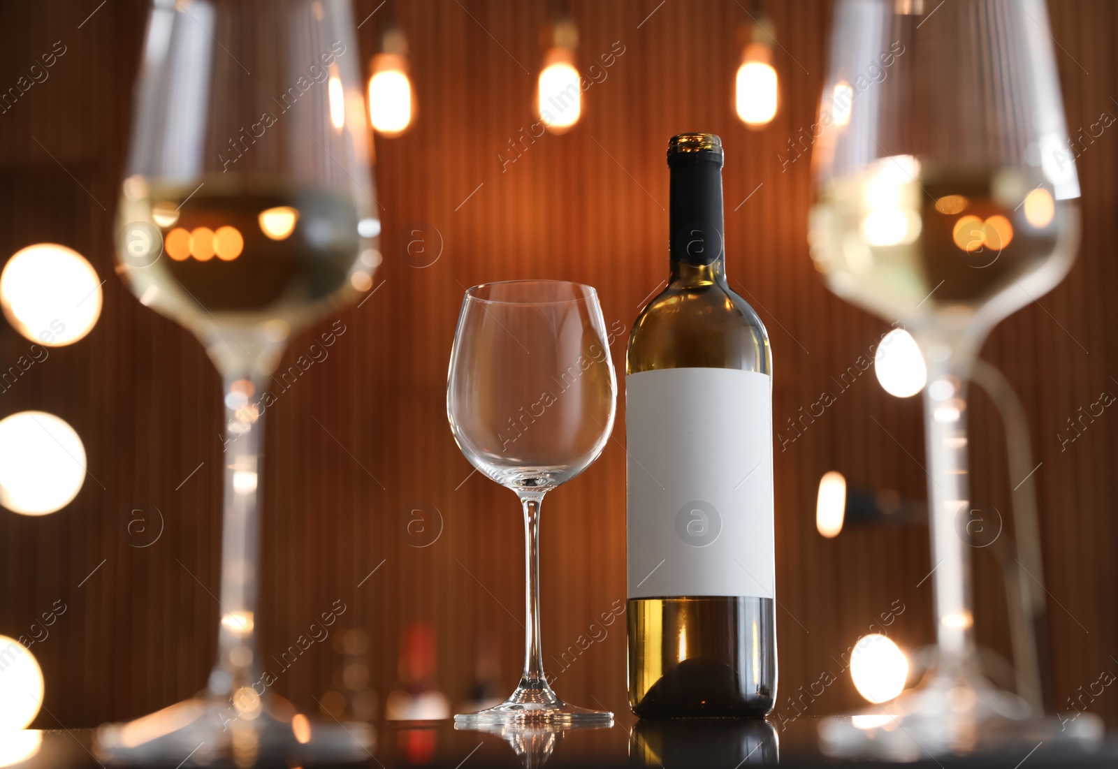 Photo of Bottle of wine and empty glass on table against blurred background. Space for text