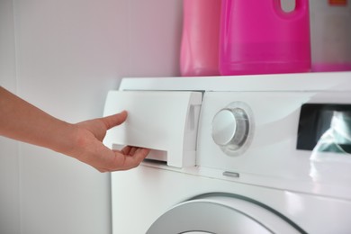 Photo of Woman opening detergent drawer of modern washing machine in bathroom, closeup