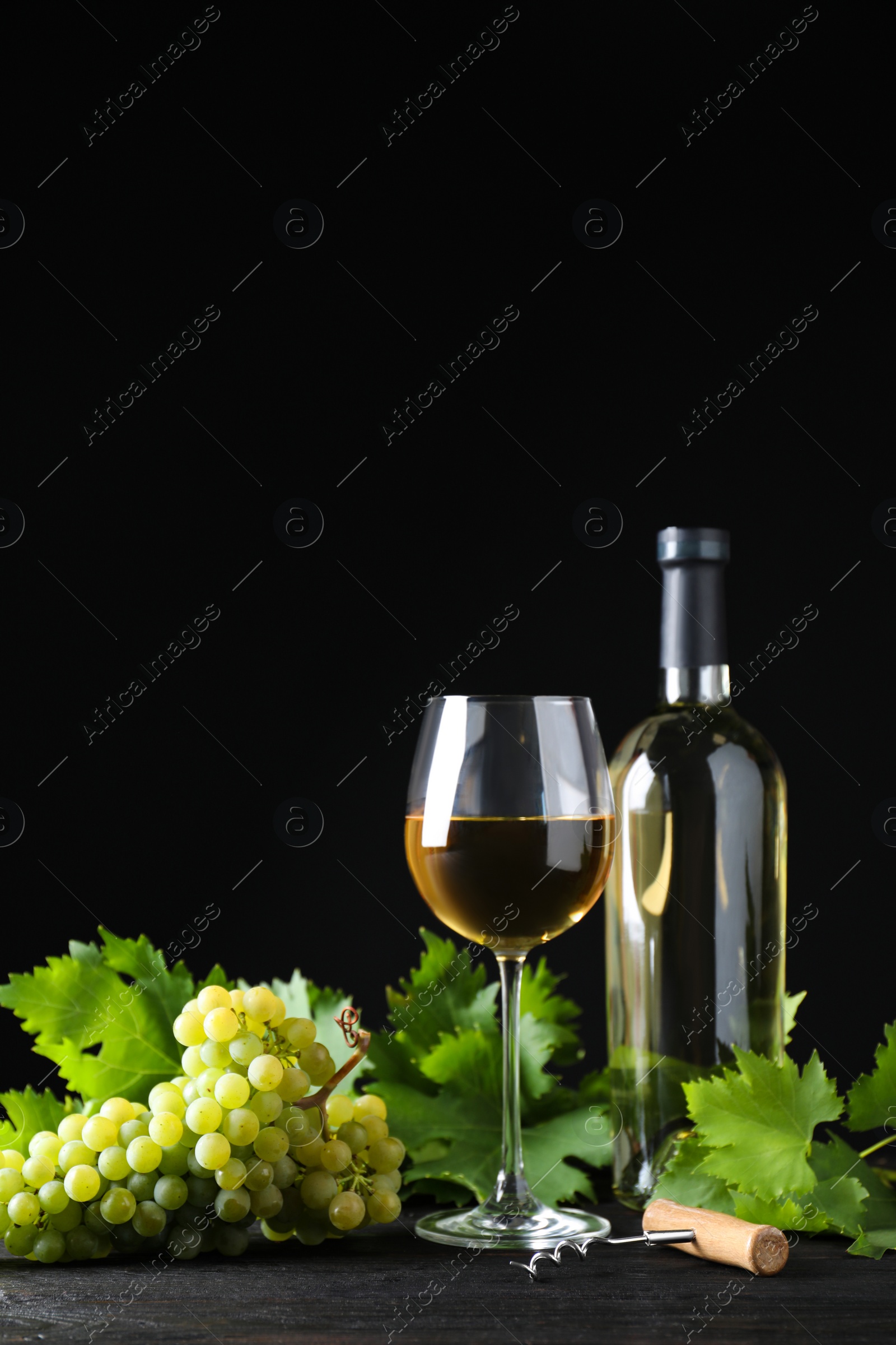 Photo of Fresh ripe juicy grapes with wineglass on grey table against black background, space for text