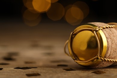 Closeup view of sparkling wine cork and muselet cap on wooden table against blurred festive lights, space for text. Bokeh effect