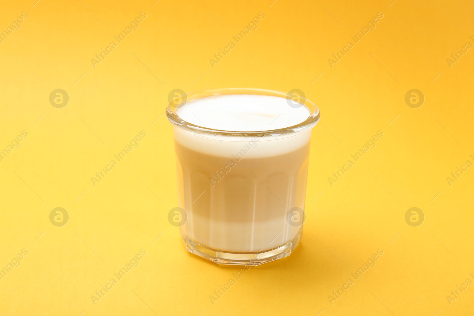 Photo of Tasty cappuccino in glass on yellow background