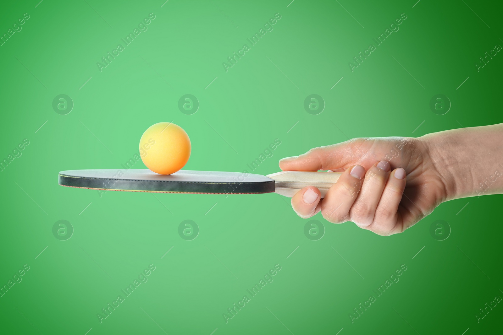 Image of Woman holding ping pong paddle with ball on green background, closeup. Table tennis championship