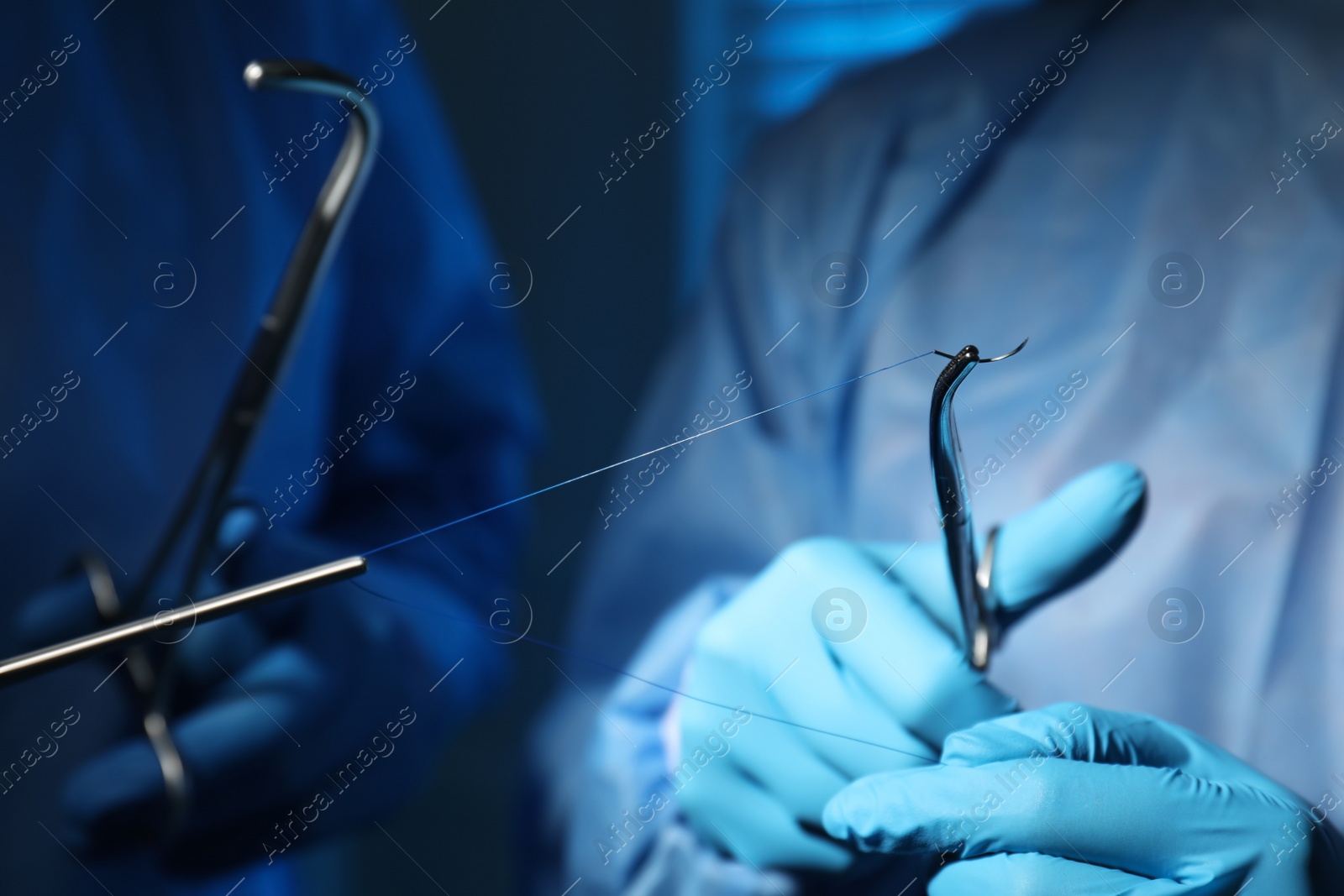 Photo of Professional surgeons with forceps and suture thread on blurred background, closeup. Medical equipment