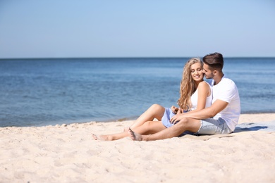 Photo of Happy young couple sitting together at beach on sunny day