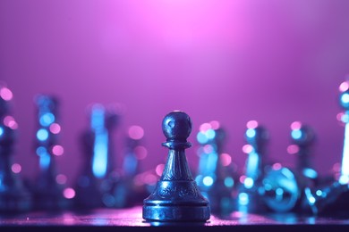 Photo of Chess pawn on checkerboard in color light, selective focus. Space for text