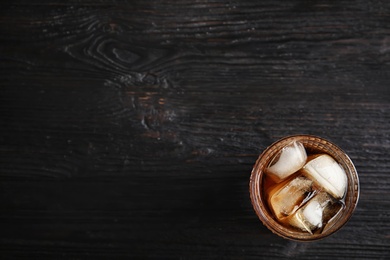 Photo of Glass of refreshing cola with ice cubes on wooden background, top view. Space for text