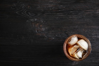 Glass of refreshing cola with ice cubes on wooden background, top view. Space for text