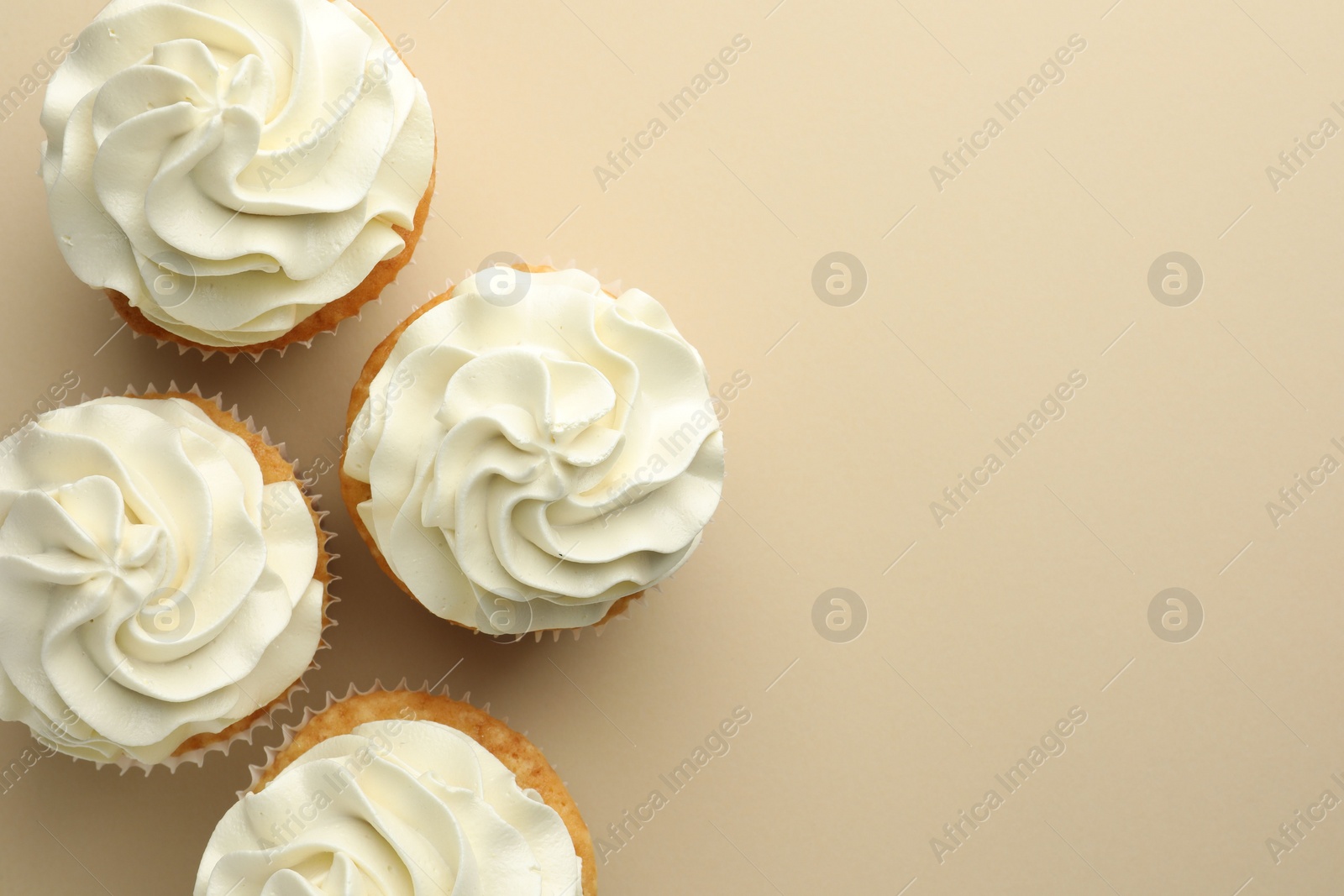 Photo of Tasty vanilla cupcakes with cream on beige background, top view. Space for text